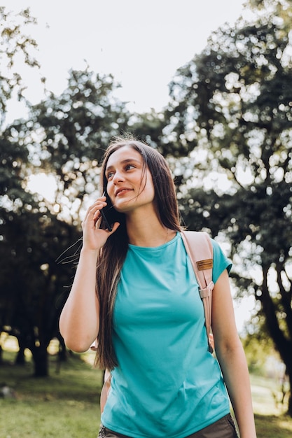 Chica estudiante adolescente con camiseta, haciendo una llamada telefónica a su familia en el parque. luz de fondo del sol