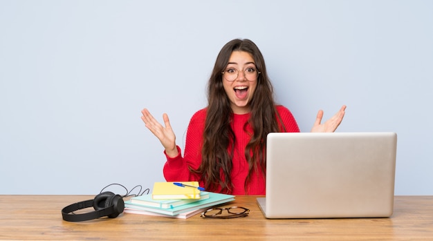 Chica estudiante adolescente estudiando en una mesa con expresión facial sorprendida