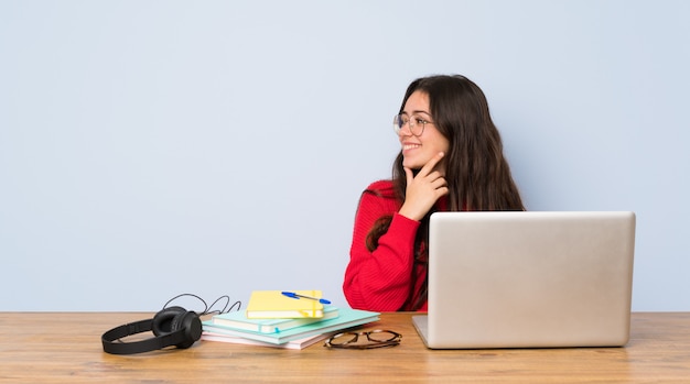 Chica estudiante adolescente estudiando en una mesa mirando hacia un lado