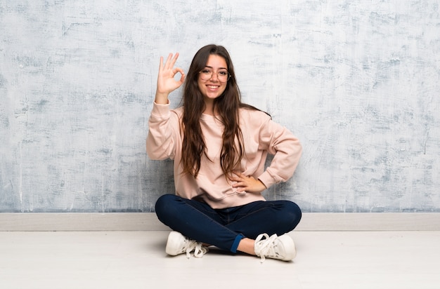 Chica estudiante adolescente estudiando en una mesa que muestra signo bien con los dedos