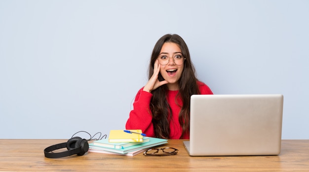 Chica estudiante adolescente estudiando en una mesa con sorpresa y expresión facial conmocionada