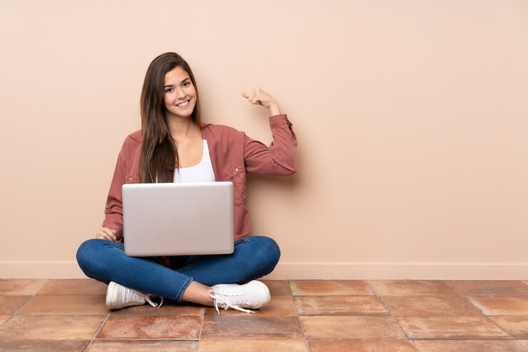 Foto chica estudiante adolescente sentada en el suelo con un portátil haciendo un gesto fuerte