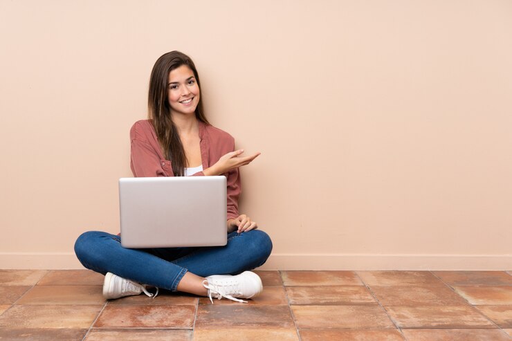 Foto chica estudiante adolescente sentada en el suelo con un portátil presentando una idea mientras mira sonriente hacia