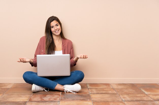 Chica estudiante adolescente sentada en el suelo con un portátil sonriendo