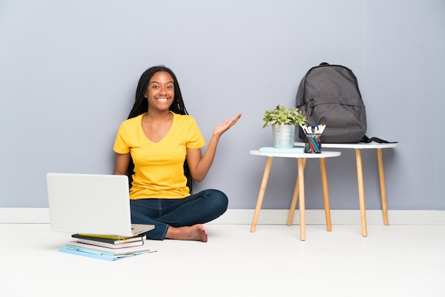 Chica estudiante adolescente sentada en el suelo sosteniendo copyspace imaginario en la palma