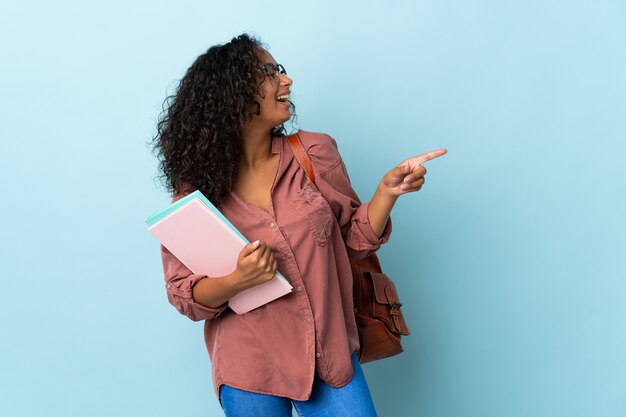 Chica estudiante aislada en azul dedo acusador hacia el lado y presentando un producto