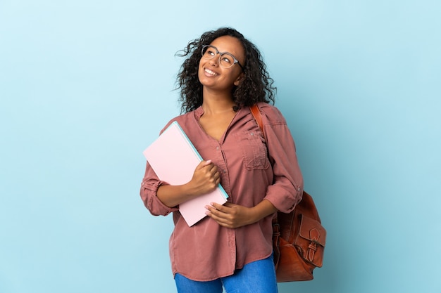 Chica estudiante aislada en azul pensando en una idea mientras mira hacia arriba