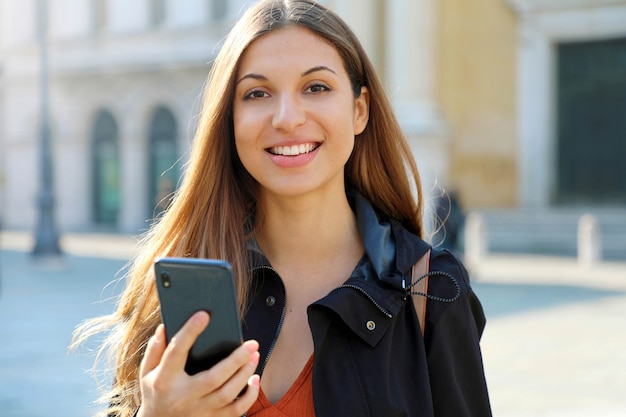 Chica estudiante alegre alegre brasileña con teléfono inteligente y mira a cámara