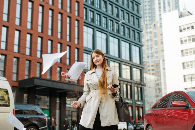 Foto chica estudiante alegre se encuentra en la calle contra el fondo del paisaje urbano