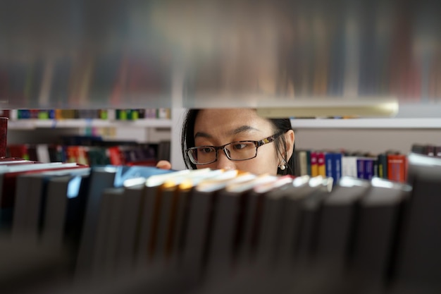 Chica estudiante asiática estudiando en la biblioteca universitaria mujer joven recogiendo un libro del estante para el proyecto