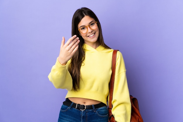 Chica estudiante brasileña adolescente sobre fondo púrpura aislado invitando a venir