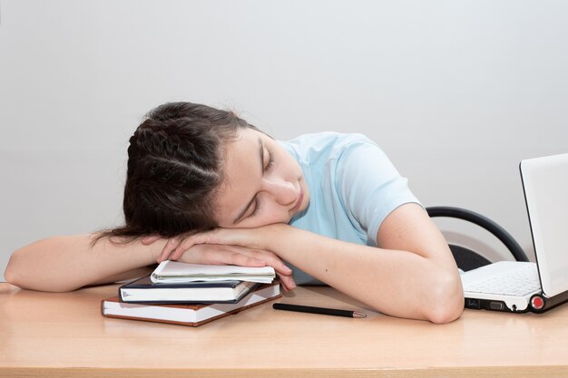 Chica estudiante cansada con libros y portátil duerme sobre la mesa.