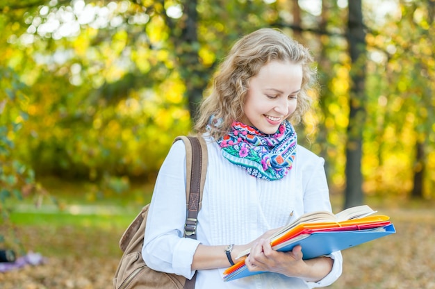 Chica estudiante está sonriendo y mirando un libro en el parque otoño