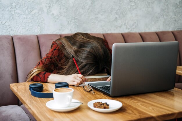 Chica estudiante estudiando examen duro y durmiendo en libros en café chica cansada trabajando