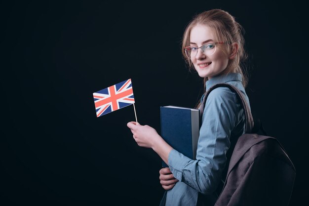 Chica estudiante feliz en gafas posando y sosteniendo la bandera británica