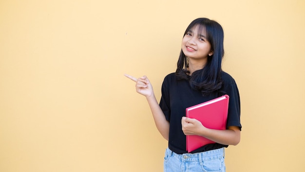 Chica estudiante feliz con libro rosa sobre fondo naranja