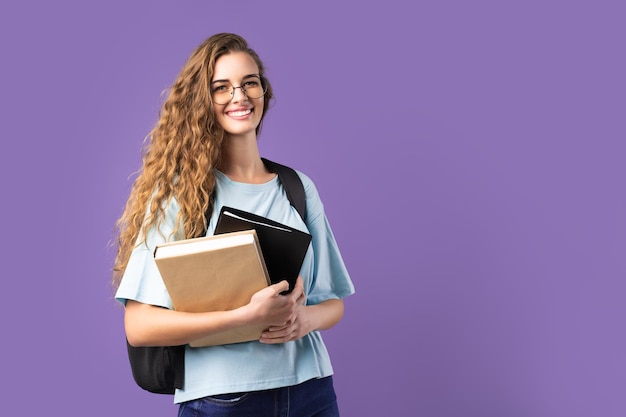 Chica estudiante feliz sostiene libros mientras mira a la cámara sobre educación de fondo blanco