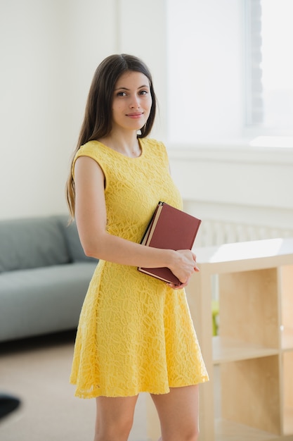 Chica estudiante hermosa inteligente con vestido amarillo sosteniendo libro