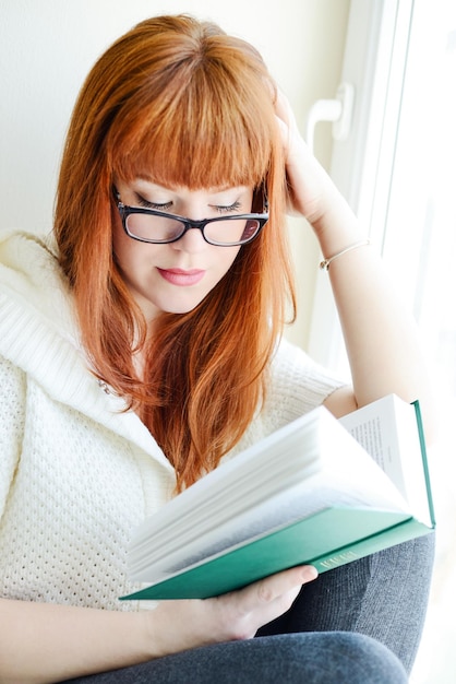 Chica estudiante de lectura con libro cerca de la ventana