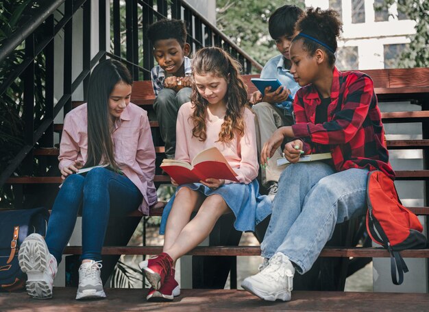 Chica estudiante leyendo un libro con amigos en el parque escolar