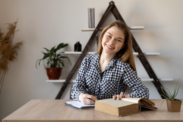 Chica estudiante en línea en una lección con un tutor remoto toma notas y estudia sin mirar a la cámara en su oficina en casa Milenial es una trabajadora independiente de Internet