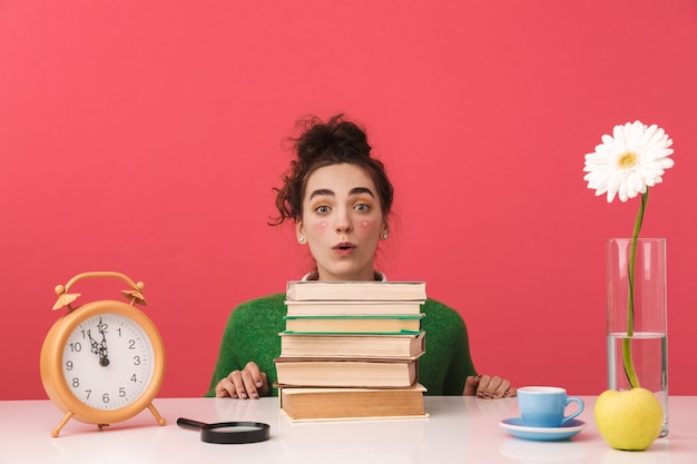 Chica estudiante nerd joven sorprendido sentado junto a la mesa con libros