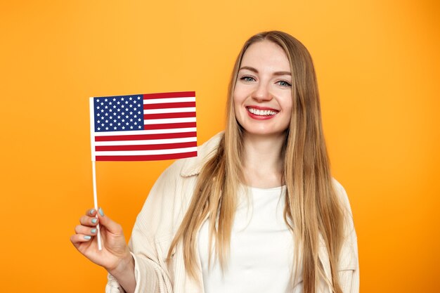 chica estudiante rubia sostiene una pequeña bandera americana y sonríe