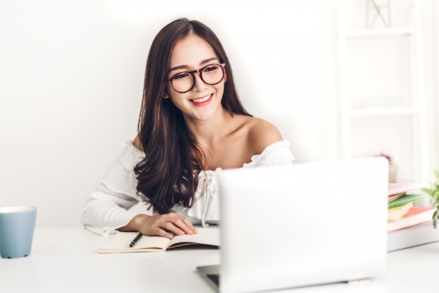 Chica estudiante sentada y estudiando y aprendiendo en línea con una computadora portátil y leyendo un libro antes del examen en casa. Concepto de educación