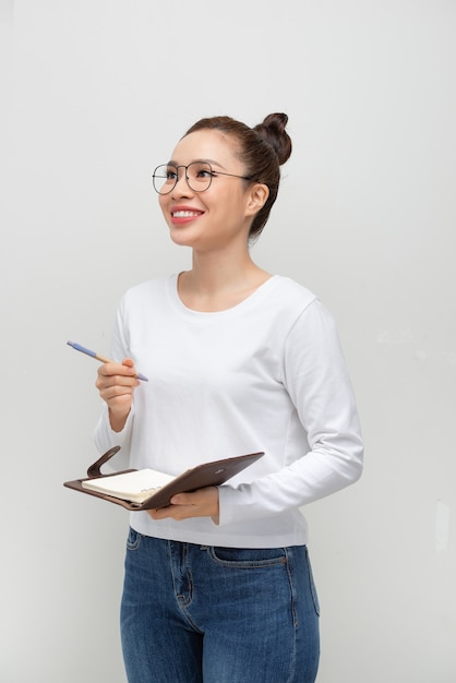 Chica estudiante seria pensativa leyendo sus notas, sosteniendo bolígrafo y cuaderno abierto