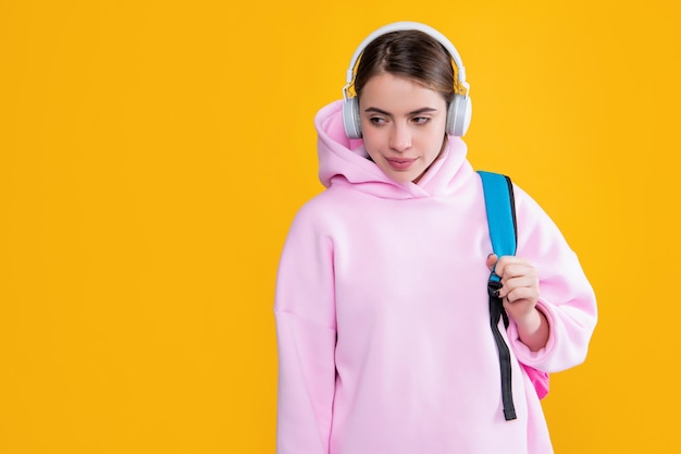 Chica estudiante sonriente en auriculares con mochila sobre fondo amarillo