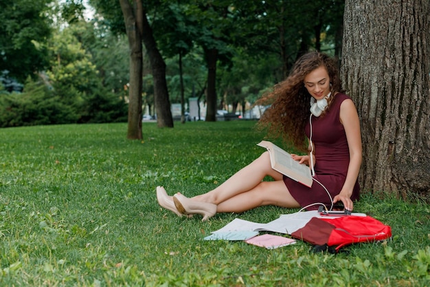 Chica estudiante sosteniendo un libro y sentada bajo un árbol