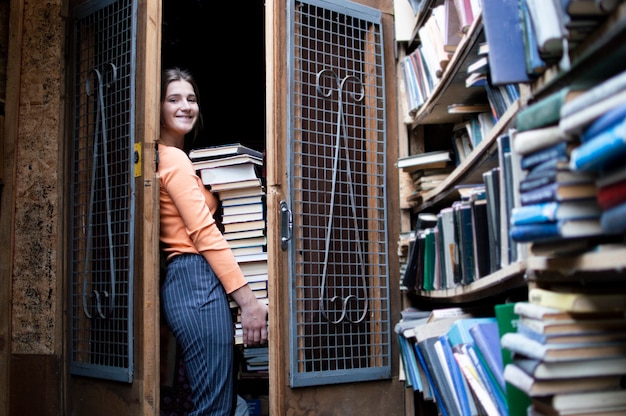 Foto chica estudiante sostiene una gran pila de libros.