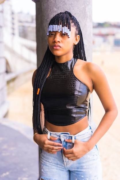 Chica étnica negra con trenzas con top de cuero y pantalón vaquero. Disfrutando de las vacaciones de verano junto a la playa