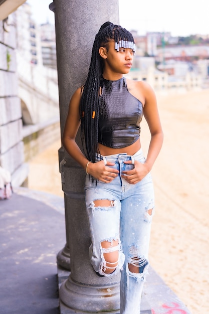 Chica étnica negra con trenzas con top de cuero y pantalón vaquero. Disfrutando de las vacaciones de verano junto a la playa