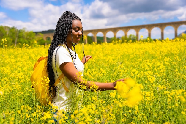 Una chica étnica negra viajera con trenzas en un campo de flores amarillas