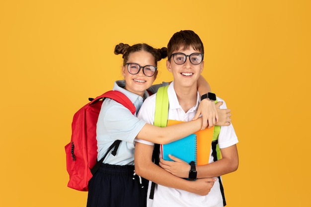 Chica europea adolescente feliz en gafas con mochila abraza a chico con cuadernos