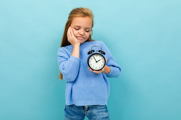 Chica europea mira un reloj despertador en la pared azul claro