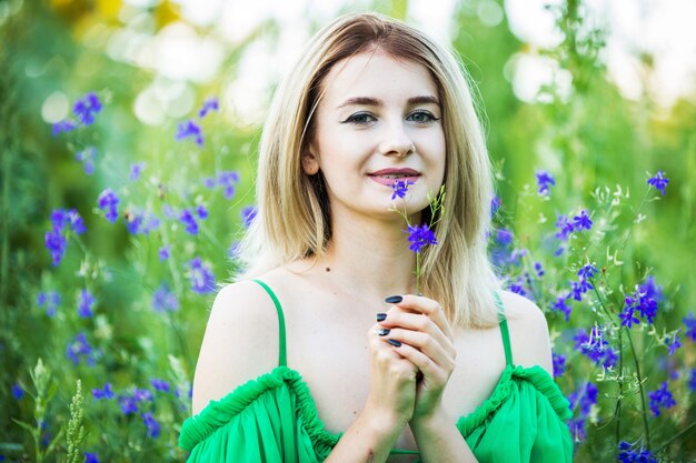 Chica europea rubia con un vestido verde en la naturaleza con flores azules