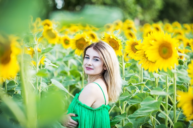 Chica europea rubia con un vestido verde en la naturaleza con girasoles