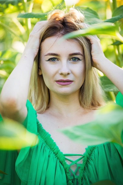 Chica europea rubia con un vestido verde en la naturaleza con girasoles