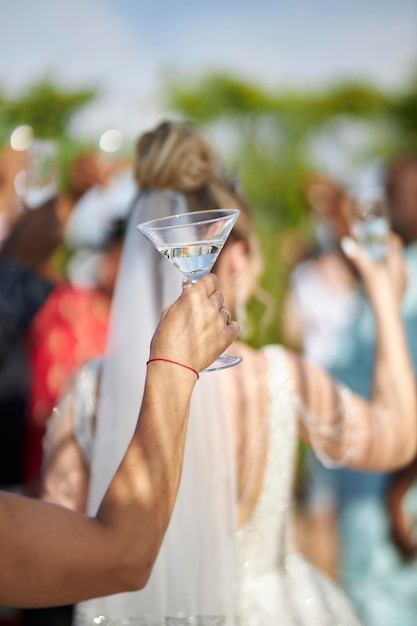una chica europea sostiene una copa de martini en las manos contra el fondo de los invitados en una fiesta de bodas