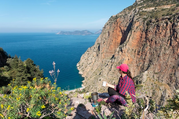 Chica excursionista bebe té sentada en una roca sobre el acantilado del valle de las mariposas La alta vista del profundo desfiladero del valle de las mariposasFethiyeTurquía