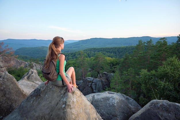 Chica excursionista descansando en la cima de una montaña rocosa disfrutando de la naturaleza matutina durante su viaje por un sendero salvaje Viajera solitaria atravesando la ruta de la cima de una colina Concepto de estilo de vida saludable