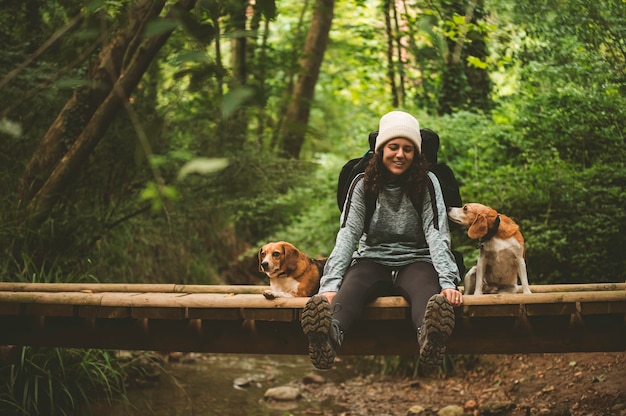 Chica excursionista descansando sobre un puente con sus perros, mirando a la cámara.