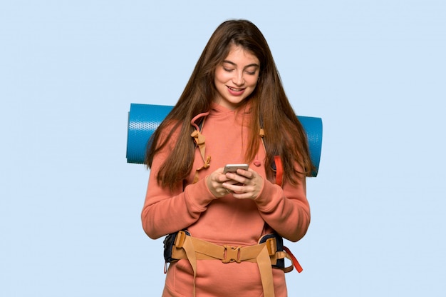 Chica excursionista enviando un mensaje con el móvil en azul