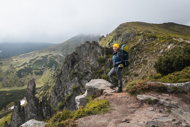 Chica excursionista con una mochila se encuentra en una roca en las montañas Vida de trekking Caminata por las montañas de los Cárpatos Verdes laderas de las montañas y rododendros en flor