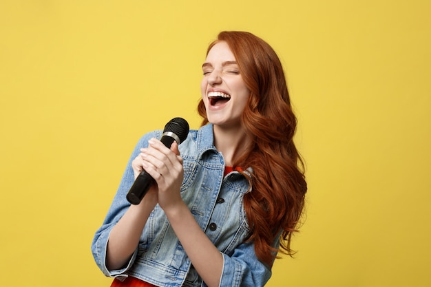 Chica expresiva cantando con un micrófono, fondo amarillo brillante aislado.