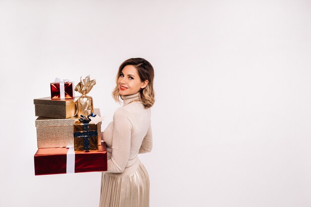 Una chica con una falda y una chaqueta con muchos regalos en sus manos sobre un fondo blanco.