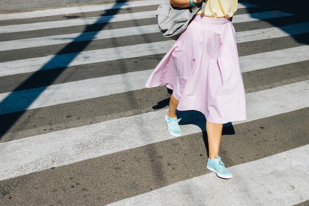 Chica en una falda rosa y zapatillas de deporte cruzando la calle en el verano