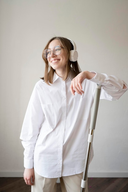 Una chica feliz con una camisa blanca con gafas y auriculares está limpiando la casa